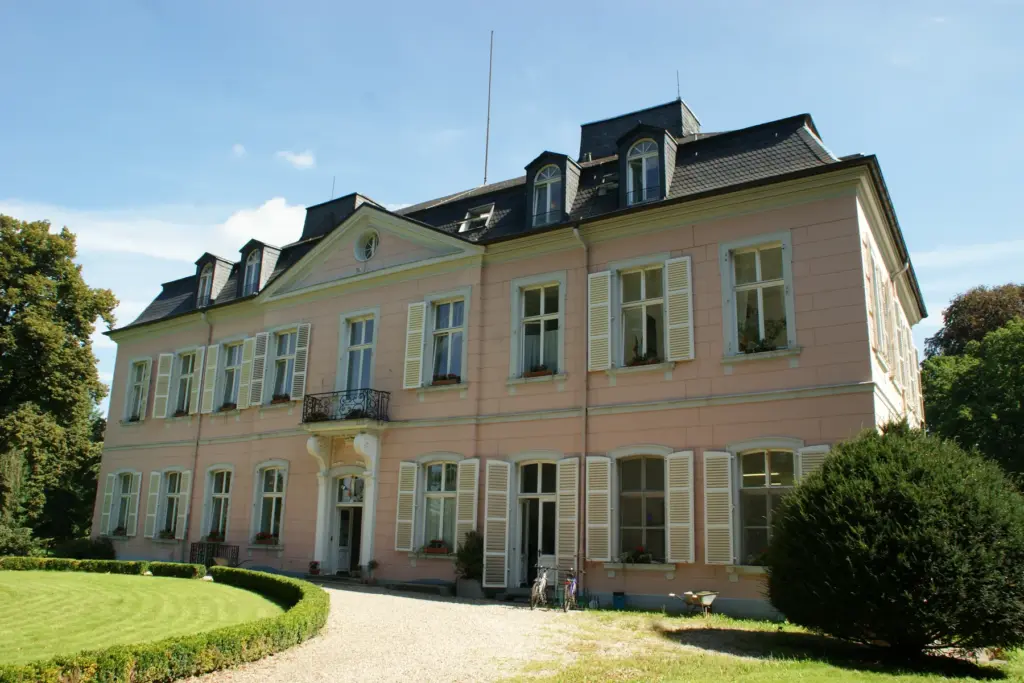 Schloss Bornheim mit rosafarbener Fassade, hellen Fensterläden und gepflegtem Rasen im Sommer