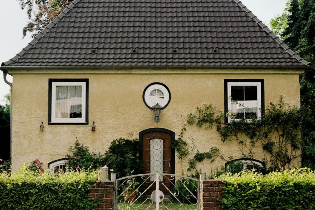 Gepflegtes Einfamilienhaus mit gelbem Putz, Walmdach, Hecke und schmiedeeisernem Gartentor