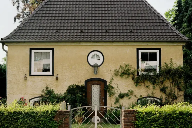 Gepflegtes Einfamilienhaus mit gelbem Putz, Walmdach, Hecke und schmiedeeisernem Gartentor