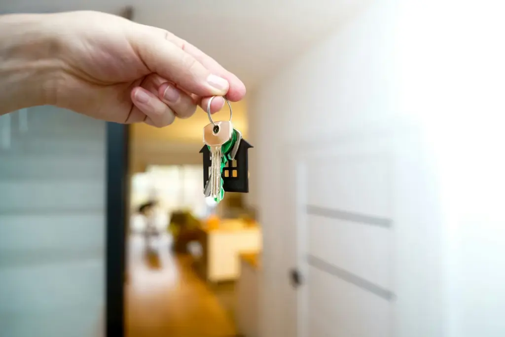 Hand hält einen Hausschlüssel mit Anhänger in Hausform vor einem hellen Flur