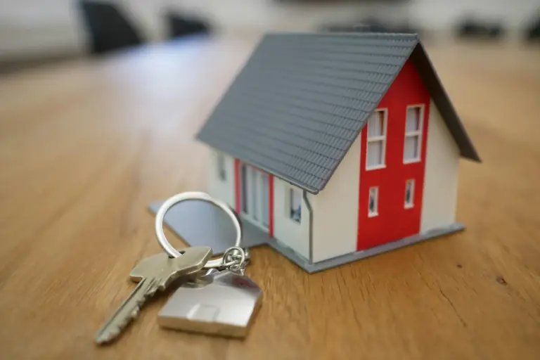 Hausmodell mit grauem Dach und Schlüssel mit Haus-Anhänger auf einem Holztisch