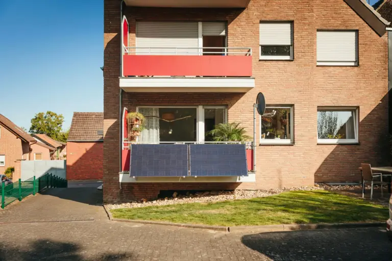 Mehrfamilienhaus aus Klinker mit Balkonen, Rollläden und gepflegtem Rasen bei Sonnenschein